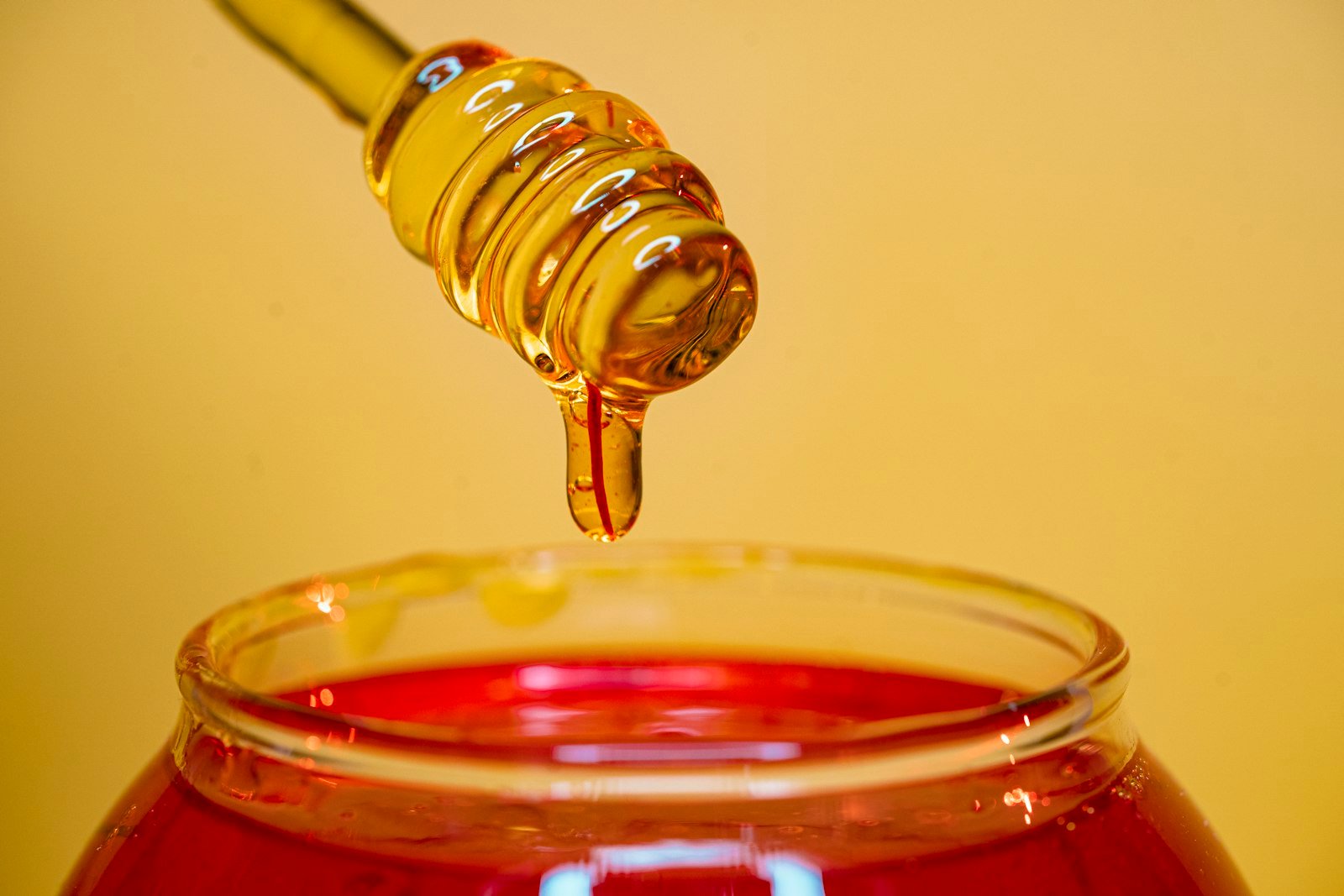 Golden pure honey dripping from a wooden honey dipper into a glass jar